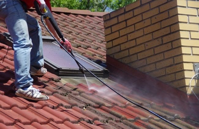 High-pressure roof cleaning by Roofing Guys Gold Coast specialists, clearing moss and grime from red roof tiles.