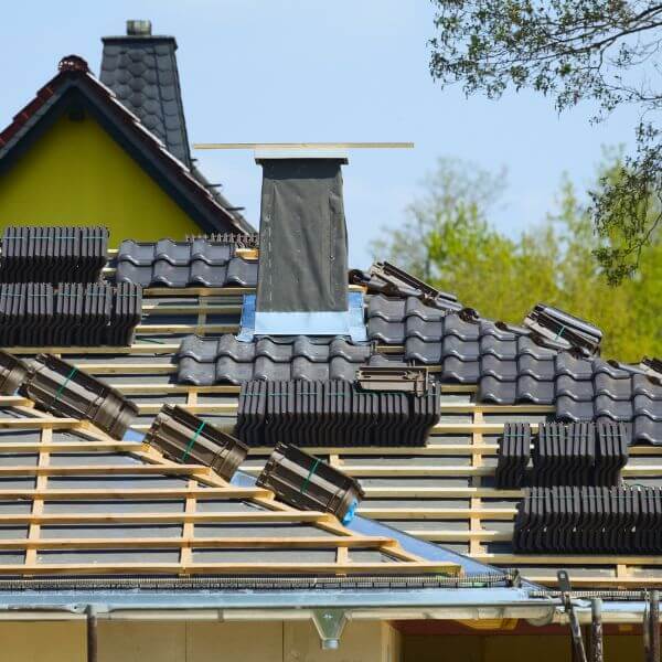 New tiled roof installation underway by Roofing Guys Gold Coast, showing roof battens, stacked tiles, and chimney flashing in progress.