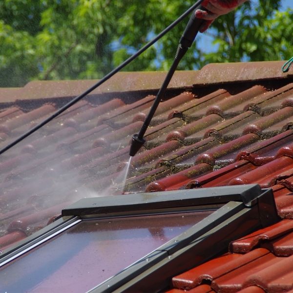 Roofing Guys Gold Coast carrying out high-pressure roof cleaning on a tiled roof to remove moss and restore its clean appearance.