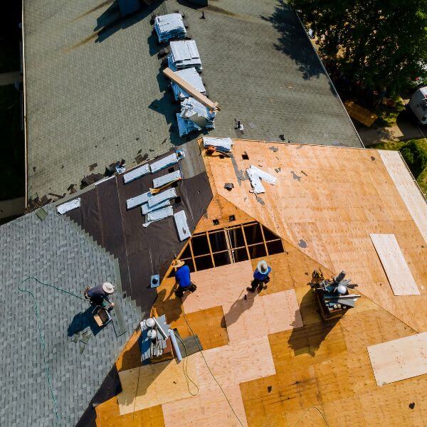 Roofing Guys Gold Coast crew installing a new roof during a home renovation project, showing exposed timber sheeting and partial shingle coverage.