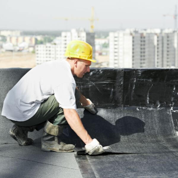Roofing Guys Gold Coast specialist applying waterproofing membrane on a commercial rooftop, part of routine strata and commercial roof maintenance services