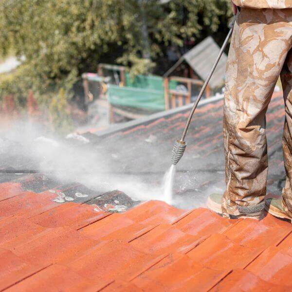 Roofing Guys Gold Coast team member pressure cleaning a tiled roof as part of a residential roof restoration.