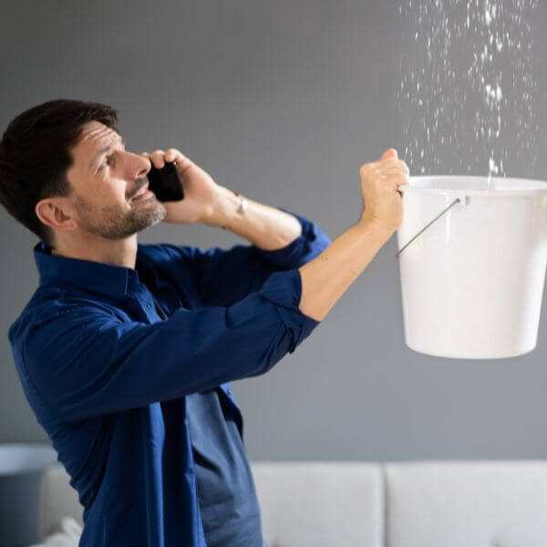Worried business owner catching water from a ceiling leak with a bucket while calling Roofing Guys Gold Coast, experts in commercial roof leak detection and repairs